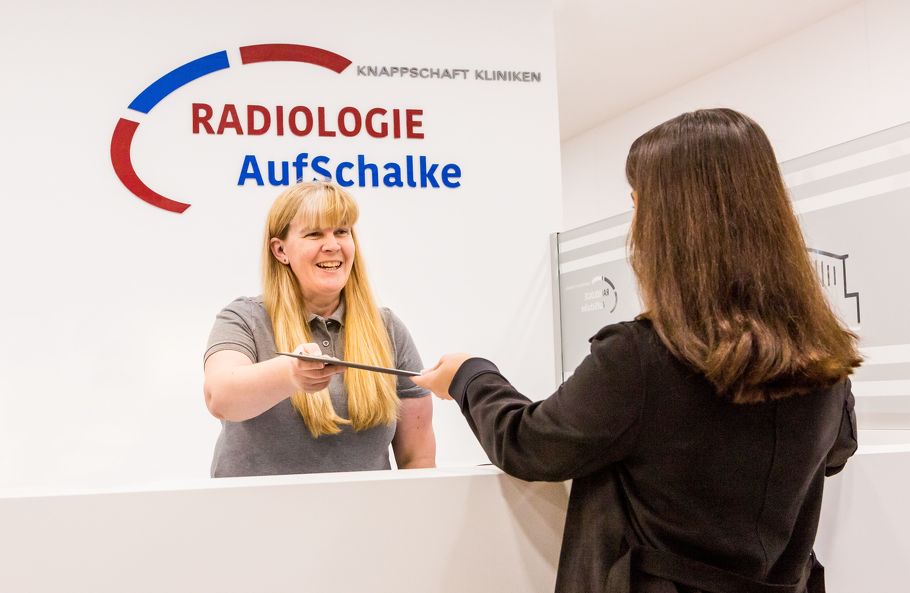 Am Patientenempfang reicht eine Praxismitarbeiterin einer Patientin ein Informationsblatt. Am Patientenempfang reicht eine Praxismitarbeiterin einer Patientin ein Informationsblatt.